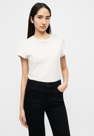 Λευκό μπλουζάκι με στρογγυλή λαιμόκοψη και κοντά μανίκια, φορεμένο μέσα σε μαύρο ψηλόμεσο τζιν, δημιουργώντας ένα απλό, κλασικό ντύσιμο.