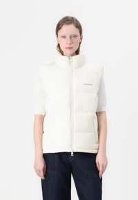 Witte gewatteerde vest met hoge kraag, ritssluiting aan de voorkant en logo aan de linkerkant. Beschikt over korte mouwen en een gladde, glanzende textuur.
