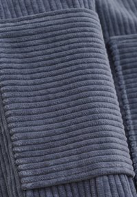 Tissu velours côtelé texturé d'un bleu profond avec un motif à côtes verticales, finition douce et bords lisses pour un aspect propre et ajusté.