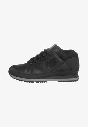 Black athletic mid-top shoes made of leather and mesh, featuring round laces, a textured logo, and a rubber sole with traction patterns.