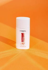 Le écran solaire Revitalift Clinical de L'Oréal dans un flacon cylindrique blanc avec un capuchon arrondi ; étiqueté SPF 50+, sur un fond orange.