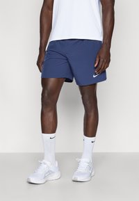 Ναυτικές αθλητικές βερμούδες Nike, από ελαφρύ ύφασμα, με πλαϊνές σχισμές, λογότυπο στο κάτω αριστερό μέρος. Φορεμένες με λευκές κάλτσες Nike και λευκά αθλητικά παπούτσια.