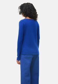 Blauer Strickpullover mit langen Ärmeln, rundem Ausschnitt und weicher Textur. Kombiniert mit passenden blauen weiten Hosen mit seitlichen Taschen.