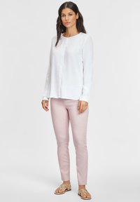 Weißes Langarm-Hemd mit Knopfverschluss, hellrosa eng anliegende Hose und goldene Sandalen. Glattes Material; das Hemd hat einen runden Halsausschnitt und eine Knopfleiste.