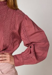 Rosa bomullsskjorta med hög krage, spetsdetaljer, veckade ärmar och intrikata broderier längs framkant och manschetter.