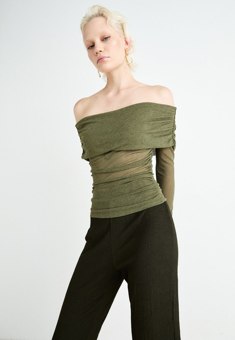 Schulterfreies, olivgrünes Oberteil mit gerafftem Mesh-Design; kombiniert mit einer dunkelgrünen, strukturierten, weiten Hose. Schlichte, moderne Schnittführung.