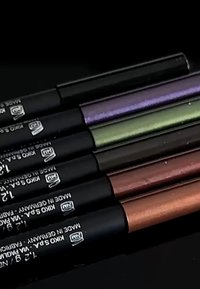 Set van zes cosmetische potloden in verschillende metallic tinten: zwart, paars, groen, bruin, brons en een lichte taupe. Elk heeft een matzwarte behuizing.