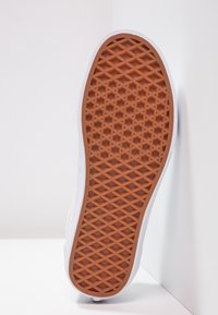 Semelle de basket blanche avec un fond en caoutchouc texturé, présentant un motif de losanges antidérapant et une semelle extérieure contrastante de couleur marron.