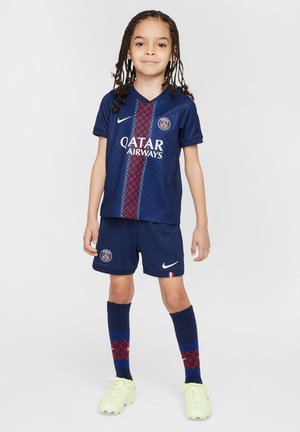 Tengerészeti futballfelszerelés, piros és fehér függőleges csíkozással, rövid ujjakkal, Nike logóval, valamint a geometrikus mintával rendelkező, hozzá illő nadrággal és zoknival.