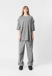 Camiseta gris de gran tamaño con mangas cortas y bolsillos, combinada con pantalones grises de corte holgado que presentan un detalle de cadena y sutiles acentos de costura.