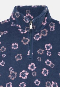 Sötétkék fleece pulóver félig cipzárral és magas gallérral, amelyen rózsaszín és világosbarna virágminták találhatók. Puha tapintás.