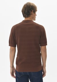 Barna rövid ujjú kötött pólóing vízszintes csíkozással és bordás gallérral. Sötétkék farmernadrággal viselve.