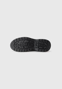 Semelle de chaussure en caoutchouc noir avec un motif de bande de roulement texturé, présentant un logo en relief pour l'adhérence et la traction. Surface lisse avec une construction durable.