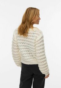Gehaakte crèmekleurige trui met golvenpatroon, voorzien van een brede ronde hals en geribbelde zoom. Zachte textuur met een losse pasvorm, gestyled met zwarte broek.