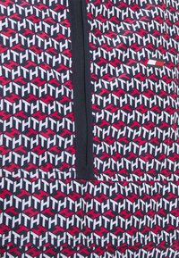 Musterpullover mit einem sich wiederholenden grafischen Design in Rot, Weiß und Schwarz, einem zentralen Reißverschluss und einer matten Oberfläche.