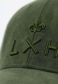 Grüne Wildledermütze mit gesticktem "LXH"-Schriftzug und einem kleinen Fleur-de-Lis-Design. Sichtbare Nähdetails verstärken die Textur.