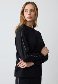 Black sweatshirt with long sleeves, a crew neckline, and metallic trim detailing along the sleeves. Smooth texture and relaxed fit.