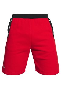 Röda idrottsshorts med ett svart elastiskt midjeband. Har sidofickor och svarta detaljer med vita accenter, inklusive en logotyp i fållen.