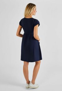 Navyblauwe jurk met korte mouwen, een aansluitend lijfje en een uitlopende rok. Has een eenvoudig ontwerp met zijzakken, gedragen met witte sneakers.
