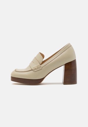 Mocassin en cuir beige avec un talon bloc en bois épais et une semelle plateforme, avec un détail de bride cousue sur la tige.