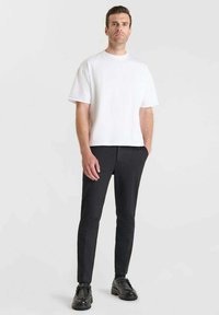 T-shirt bianca in cotone con maniche corte, abbinata a pantaloni neri skinny. Le scarpe sono in pelle nera. Design semplice, senza motivi.