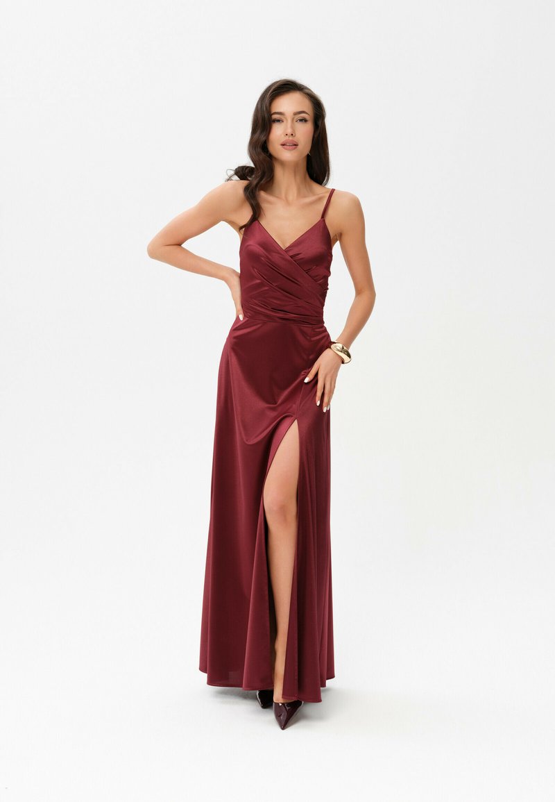 Burgundské saténové večerní šaty s přiléhavým tělem, překládaným designem, tenkými ramínky a rozparkem až po stehna. Dokončeno s lodičkami s špičatou špičkou.