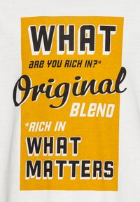 Valge t-särk, millel on julged mustad ja kollased tekstid. Disain sisaldab fraase nagu "Milles oled rikastunud?" ja "Originaalne segu."