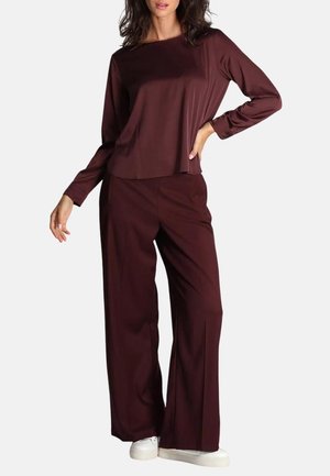 Top bordeaux a maniche lunghe e pantaloni a gamba larga in tessuto morbido. L'outfit è abbinato a sneaker bianche, caratterizzate da una silhouette rilassata.