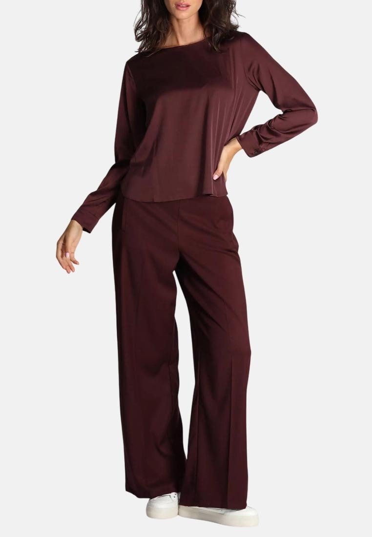 Top bordeaux a maniche lunghe e pantaloni a gamba larga in tessuto morbido. L'outfit è abbinato a sneaker bianche, caratterizzate da una silhouette rilassata.