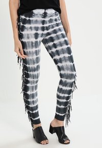 Leggings tie-dye noir et blanc avec un design ajusté et des franges sur le côté. Fabriqués à partir d'un matériau extensible et lisse.