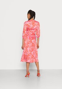 Vestido multicolorido com um padrão abstrato em rosa e laranja ousado, com mangas a três quartos e barra ampla. Combinado com saltos laranja.