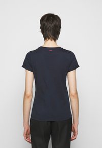 Mörkblå t-shirt i bomull med korta ärmar, rund halsringning och en liten röd logga på nacken bak. Slät textur, figurnära passform.