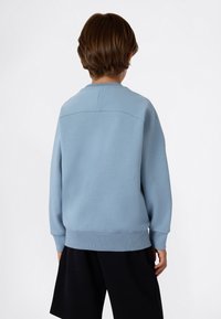 Sweatshirt bleu clair avec des poignets et un ourlet côtelés, présentant un col rond et un tissu texturé. La vue de dos montre des coutures lisses et une coupe décontractée.