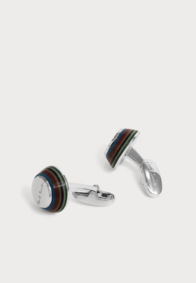 Paire de boutons de manchette ronds en argent avec des bords rayés multicolores et le nom de la marque gravé sur des faces lisses, reposant sur une surface blanche.