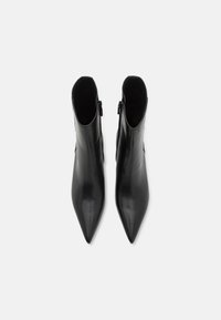 Botas de tornozelo em couro preto com bico fino e um design elegante. Fecho lateral com zip e textura suave sem padrões visíveis.
