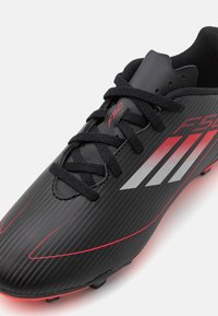 Scarpe da calcio nere con una parte superiore testurizzata e accenti rossi, tre strisce argentate e lacci neri. Progettate per le prestazioni sul campo.