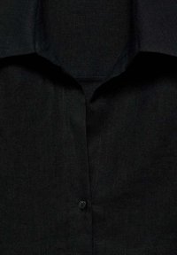 Cămașă neagră cu guler întins, dintr-un material texturat, și un singur nasture negru la gât.