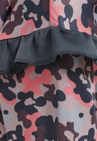Falbaniasty materiał w różowym, czarnym i beżowym wzorze kamuflażu. Teksturowana powierzchnia z gładkimi i falbaniastymi krawędziami, zaprojektowana do warstwowego noszenia.