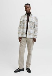 Camisa de franela a cuadros en gris, beige y blanco, con dos bolsillos en el pecho. Combinada con pantalones de pana beige y zapatos negros de cordones.
