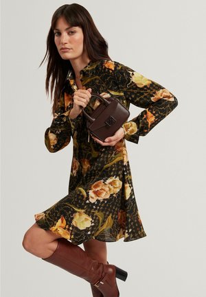 Zwarte bloemenjurk met lange mouwen, met oranje en gele bloemen, gecombineerd met een donkerbruine rechthoekige handtas.