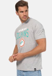 Šedé bavlněné tričko s grafikou Miami Dolphins v tealové a oranžové barvě, krátké rukávy, kulatý výstřih a štítek s logem na lemu.