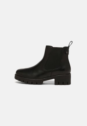 Zwarte leren enkellaars met een chunky zool, elastisch zijpaneel, lage hak en een trekband aan de achterkant op een witte achtergrond.