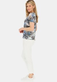 Koszula z krótkim rękawem w niebiesko-brązowy wzór tropikalnych liści; zestawiona z białymi spodniami 3/4 i białymi trampkami. Gładka faktura.