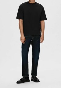 Černé tričko s krátkým rukávem, volný střih, nošeno s tmavě modrými rovně střiženými džíny a černými botami se hladkým lesklým povrchem.
