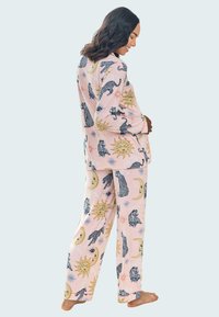Ljusrosa pyjamasset med en blandning av sol-, måne- och djurmönster i svart och guld. Tillverkad av mjukt material med en avslappnad passform.