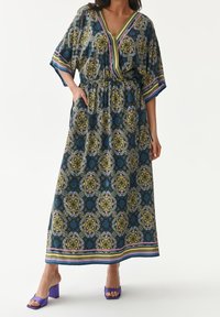Maxikleid mit floralem Muster in Grün-, Blau- und Lilatönen; V-Ausschnitt, elastischer Bund und kurze Ärmel. Kombiniert mit lila Blockabsätzen.
