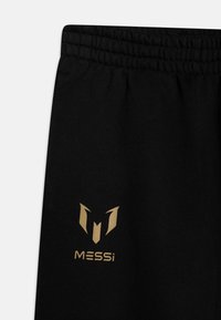 Sorte joggers med elastisk talje. Har et guld logo med en stiliseret "M" og teksten "MESSi" trykt på venstre side.