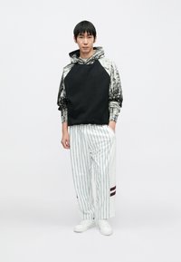 Czarna i szara bluza z kapturem w wzory z raglanowymi rękawami, zestawiona z białymi spodniami w paski z bordowymi akcentami oraz białymi trampkami.