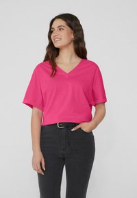 Fuchsiové v-neck tričko s krátkými rukávy, vyrobené z měkké bavlny, v kombinaci s černými vysokými džíny a černým pásem.