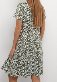 Zielona sukienka z białym abstrakcyjnym wzorem, krótkimi rękawami, rozkloszowanym fasonem i gładką, tkana strukturą.